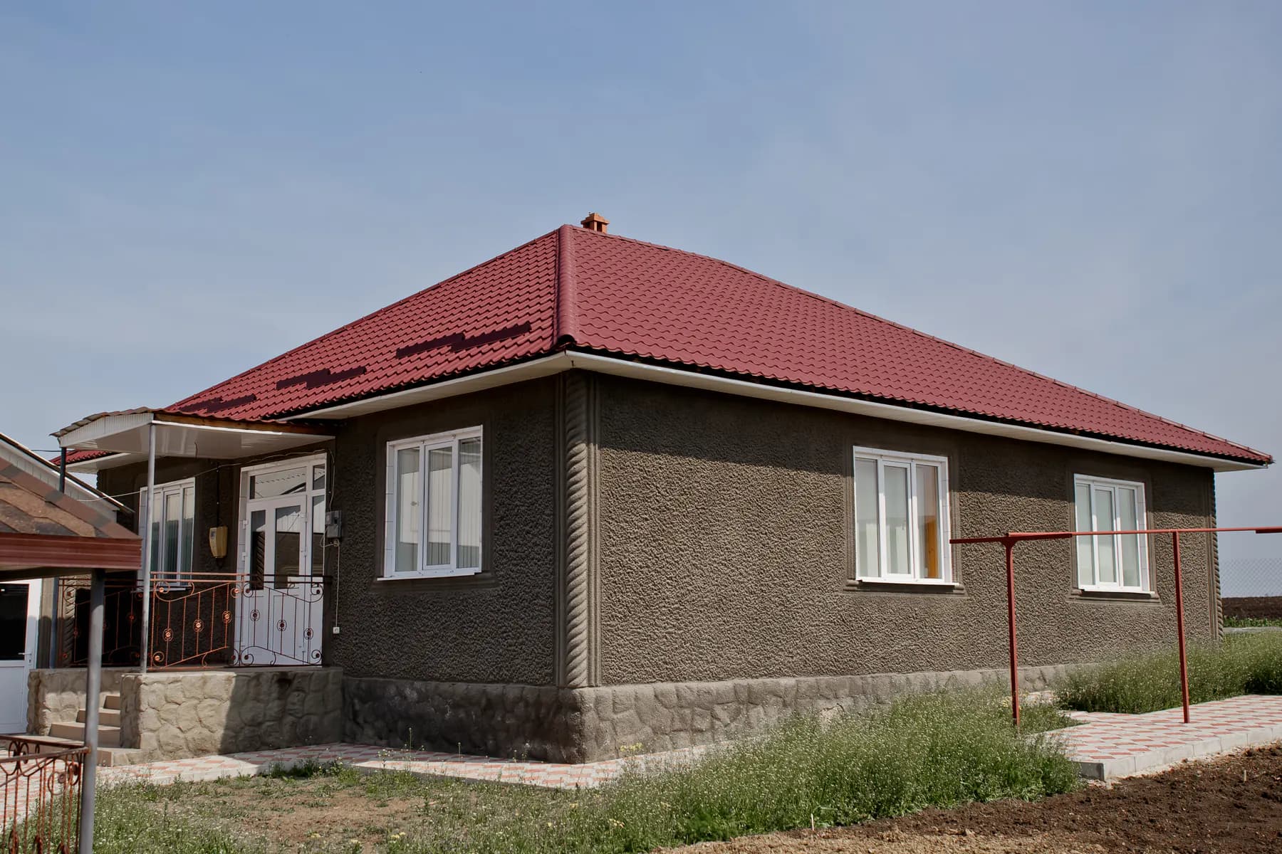 Casă cu un nivel, cu fațadă tencuită texturat în gri închis și acoperiș în patru ape din țiglă metalică roșie