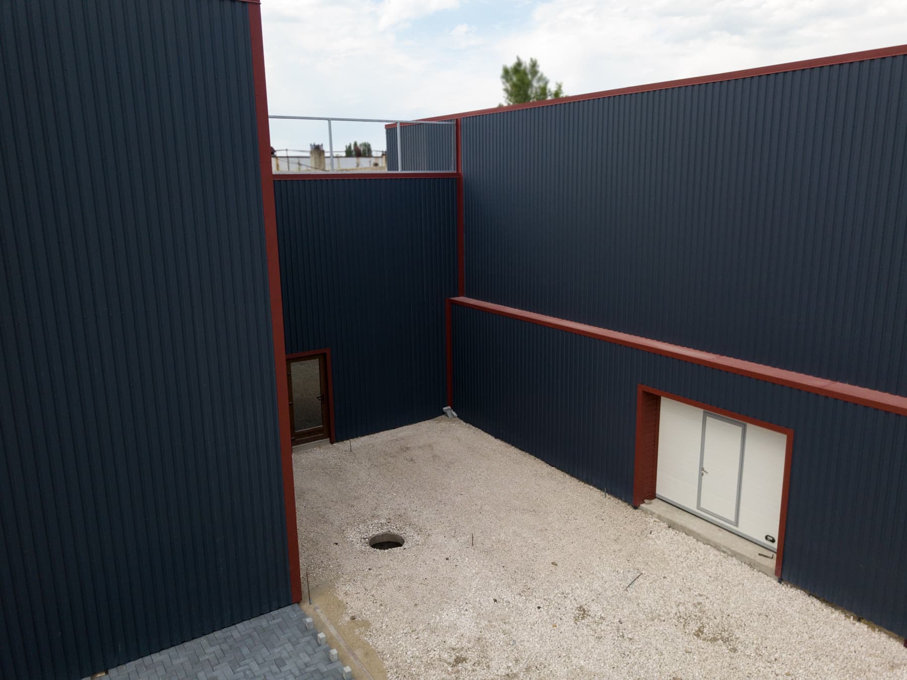 Clădire industrială placată cu tablă profilată gri închis cu borduri roșii, văzută de sus, în jurul unei curți interioare